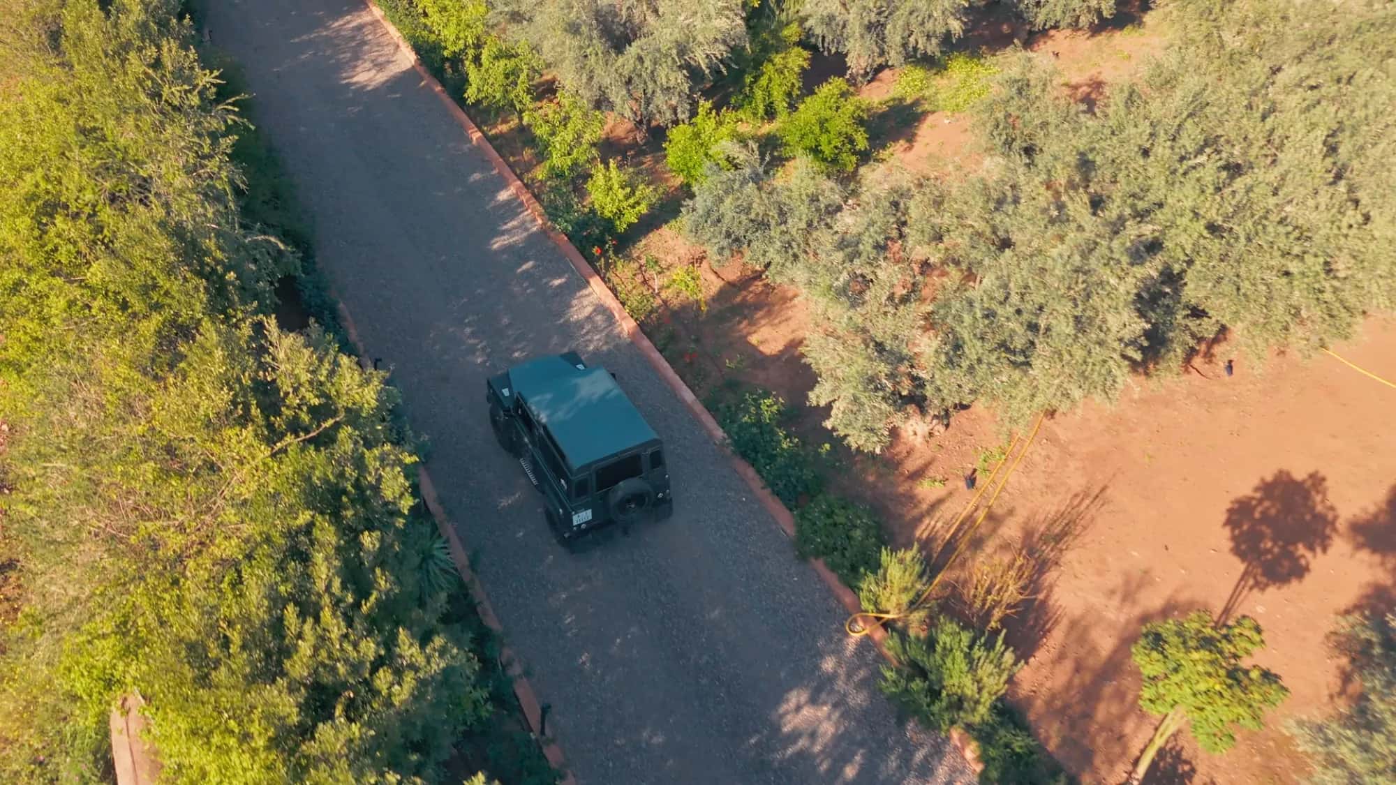 Aerial view of a black 4x4 arriving at Villa Yemna in Marrakech along the driveway lined with green hedges and olive trees.