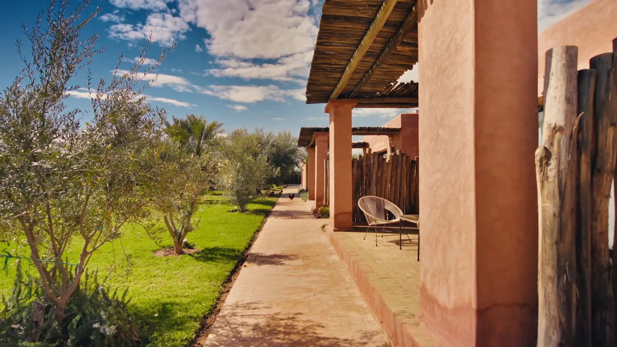 Reed pergola of a bungalow suite at Villa Yemna in Marrakech with rattan chair, olive trees and lawn.
