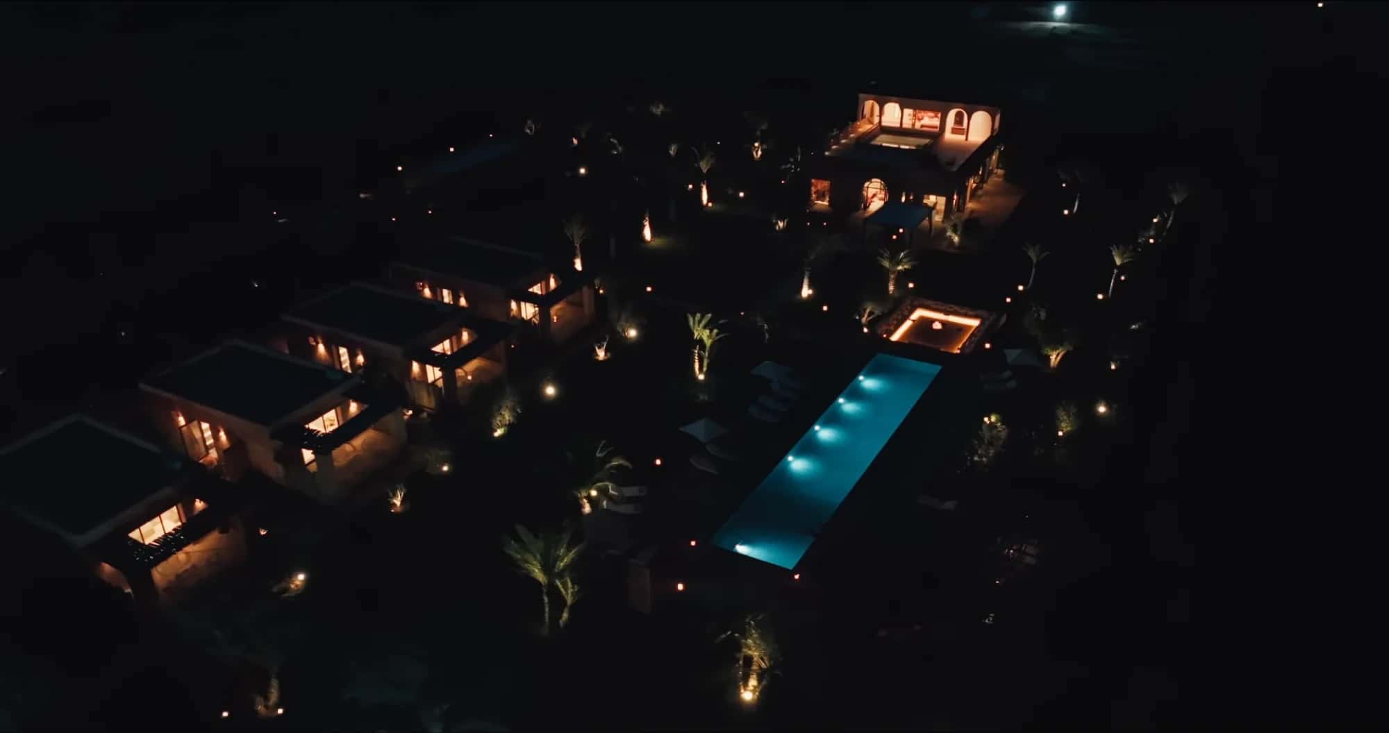 Aerial night view of the Villa Yemna estate in Marrakech illuminated: riad, bungalow suites, pool and gardens lit under the starry sky.