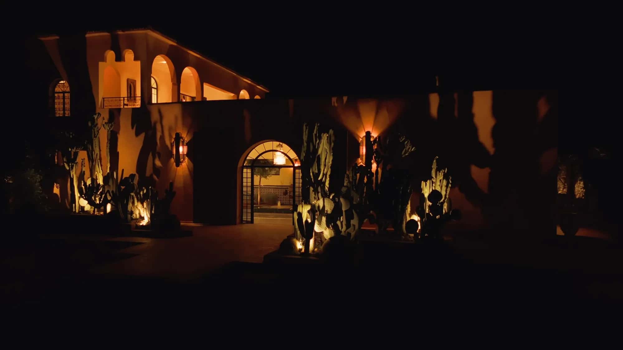 Villa Yemna façade at night in Marrakech with illuminated arched entrance, uplit cacti and bronze sconces.