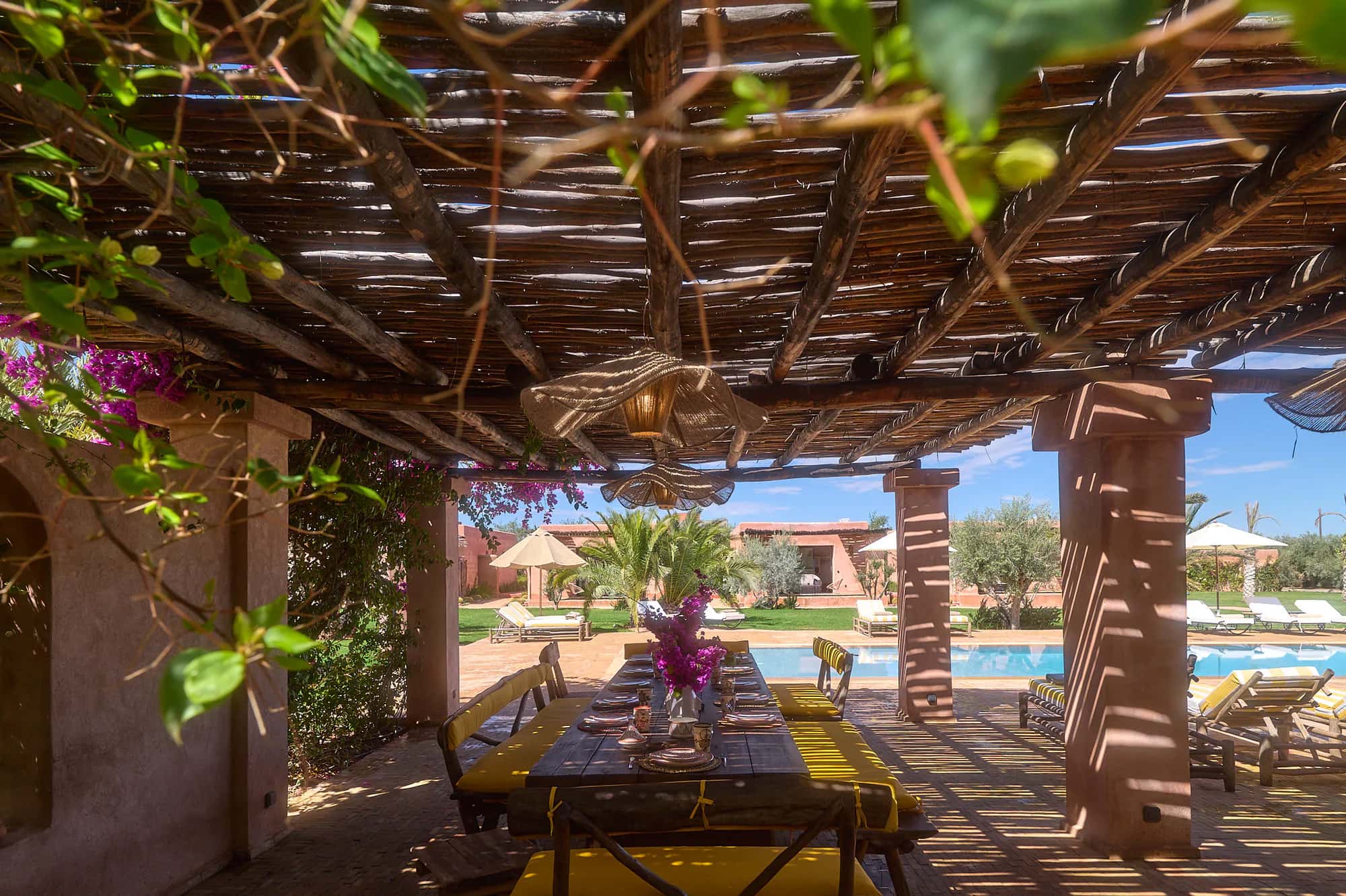 Shaded pergola dining area at Villa Yemna with a set table, bougainvillea flowers, and views of the pool and gardens.