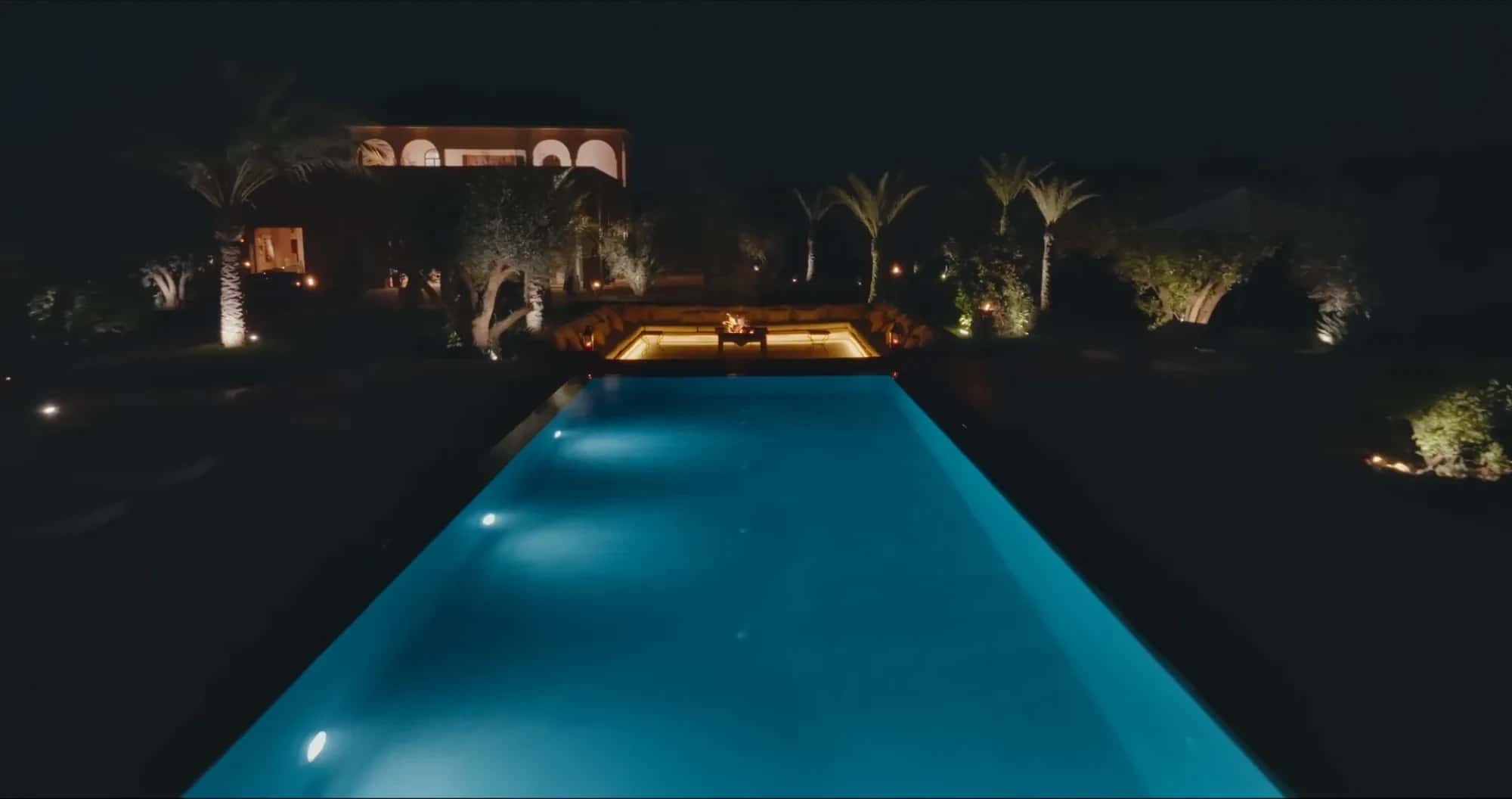 Villa Yemna pool in Marrakech illuminated at night, with lit riad in the background and palm trees.