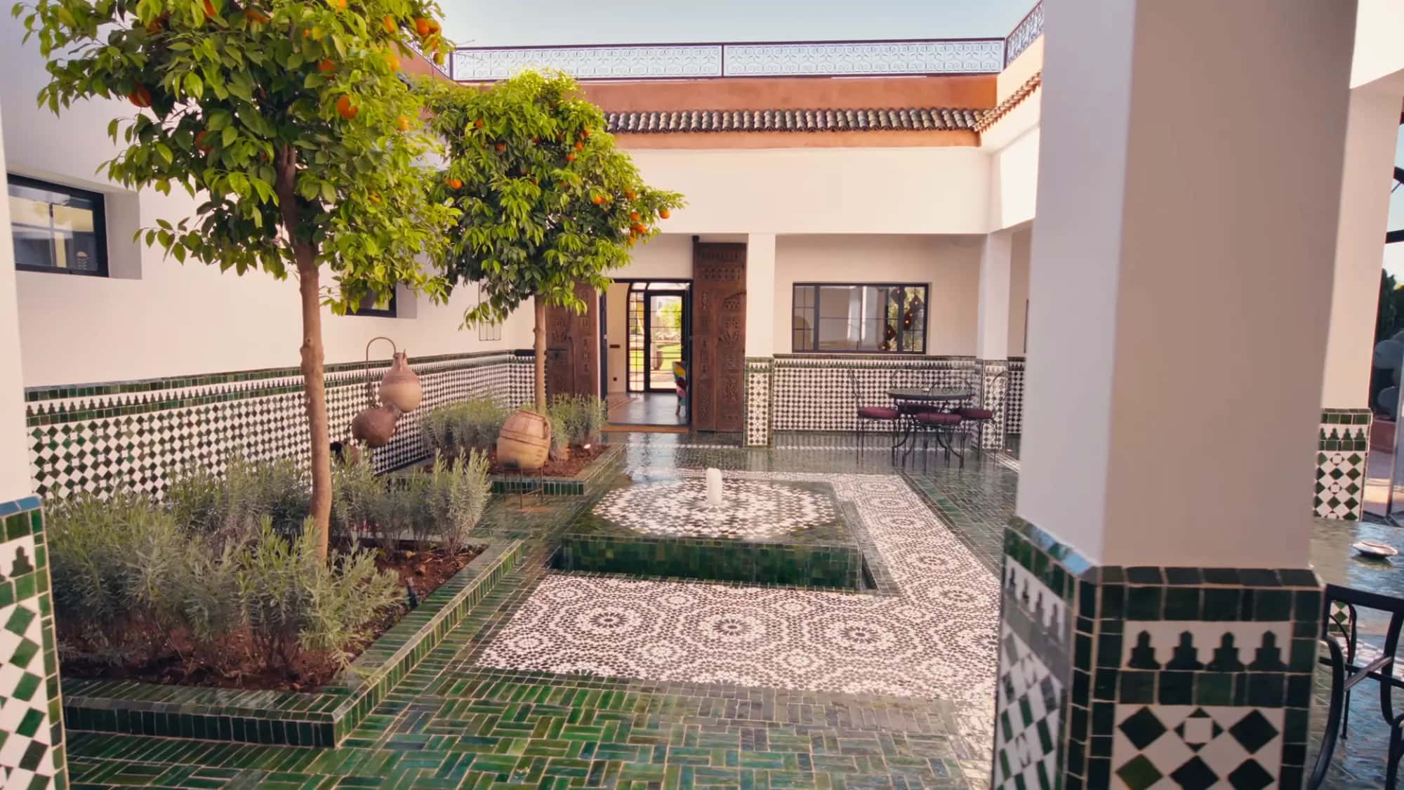 Inner courtyard of the Villa Yemna riad in Marrakech with central fountain, glossy green zellige floor, orange tree and traditional Moroccan arcades.
