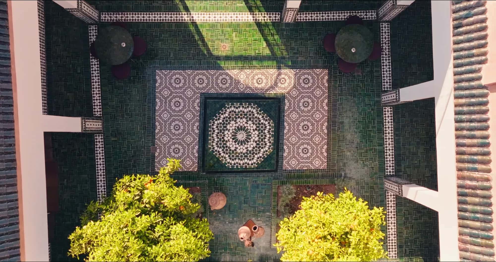 Top-down view of the Villa Yemna riad courtyard in Marrakech, with intricate zellige flooring featuring Moroccan rosettes and potted orange trees.