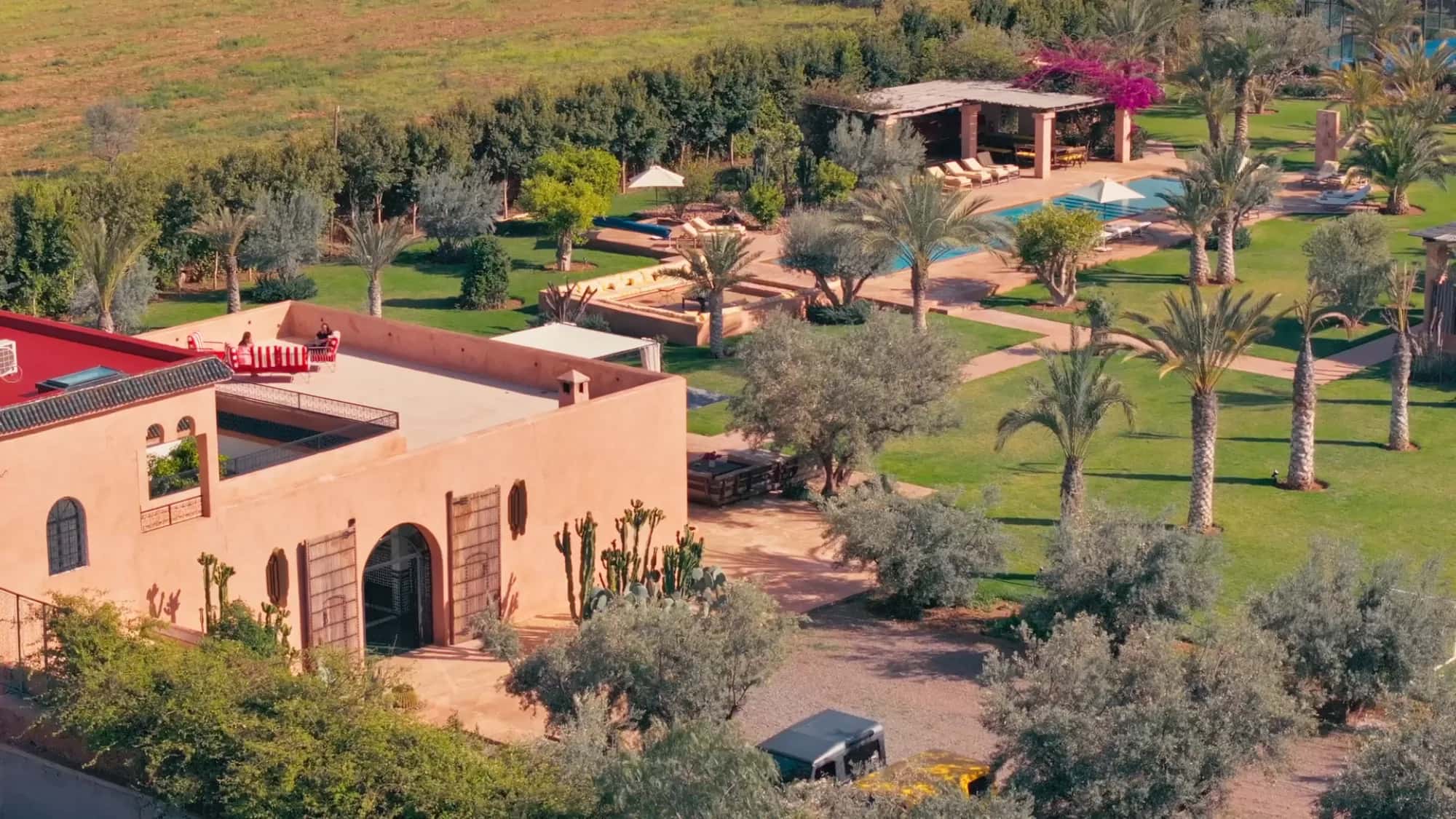 Aerial view of the Villa Yemna riad in Marrakech with adjacent pergola, pool, olive grove and rooftop terrace at golden hour.