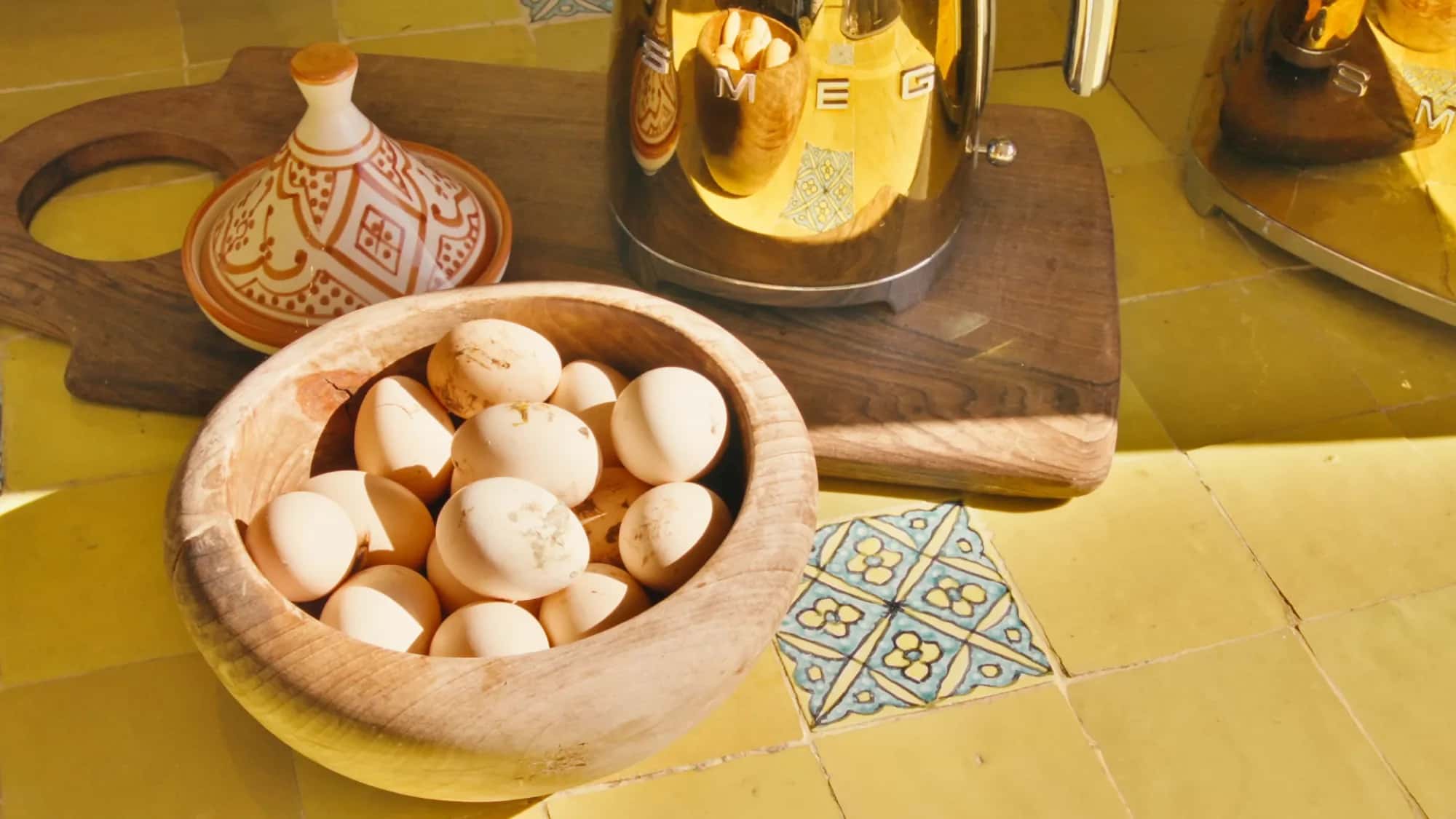 Kitchen detail at the Villa Yemna riad with wooden bowl of fresh eggs, gold SMEG kettle and yellow zellige countertop.
