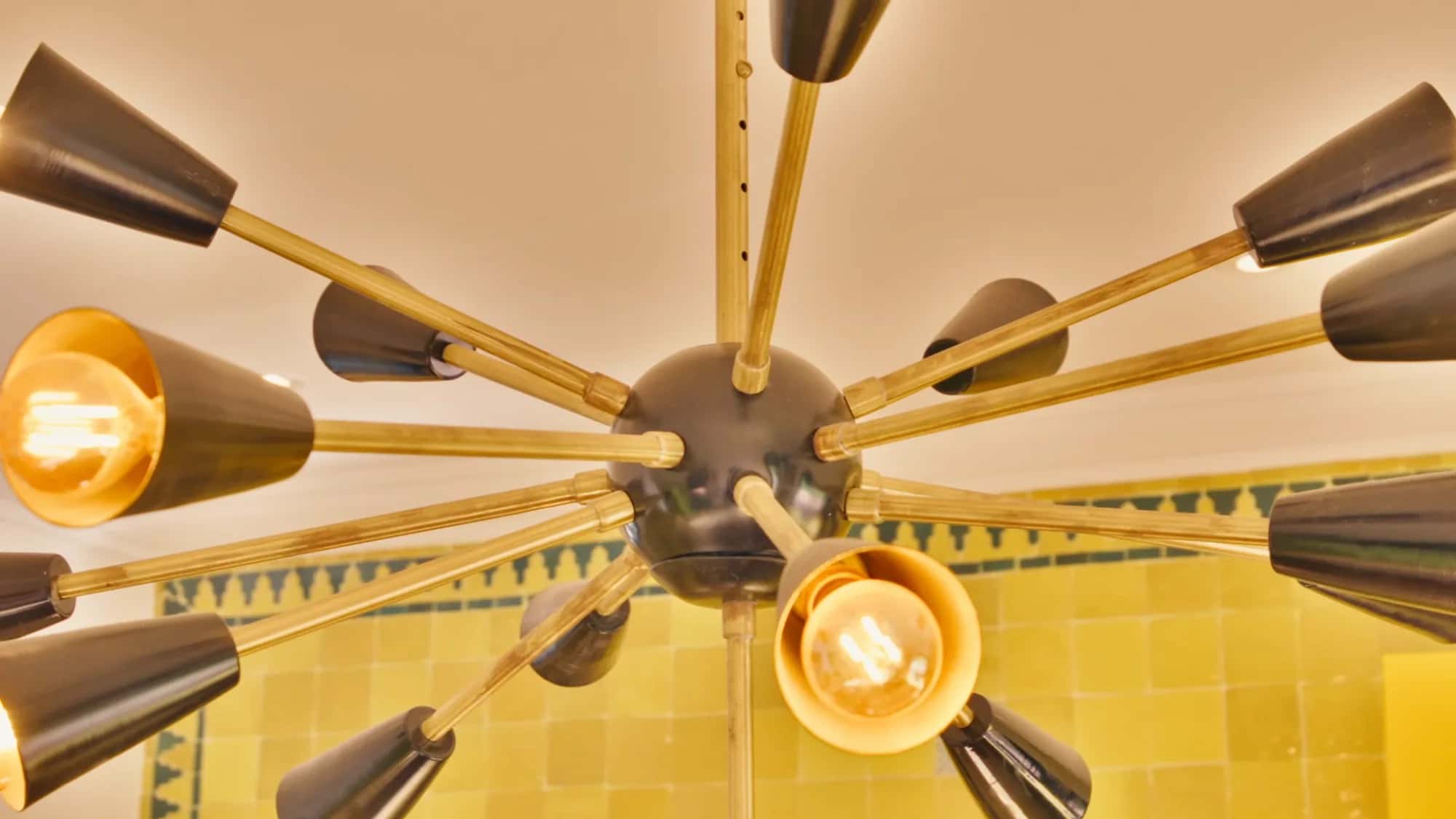 Close-up of the modern sputnik chandelier in the Villa Yemna riad kitchen in Marrakech, against yellow zellige tiles.