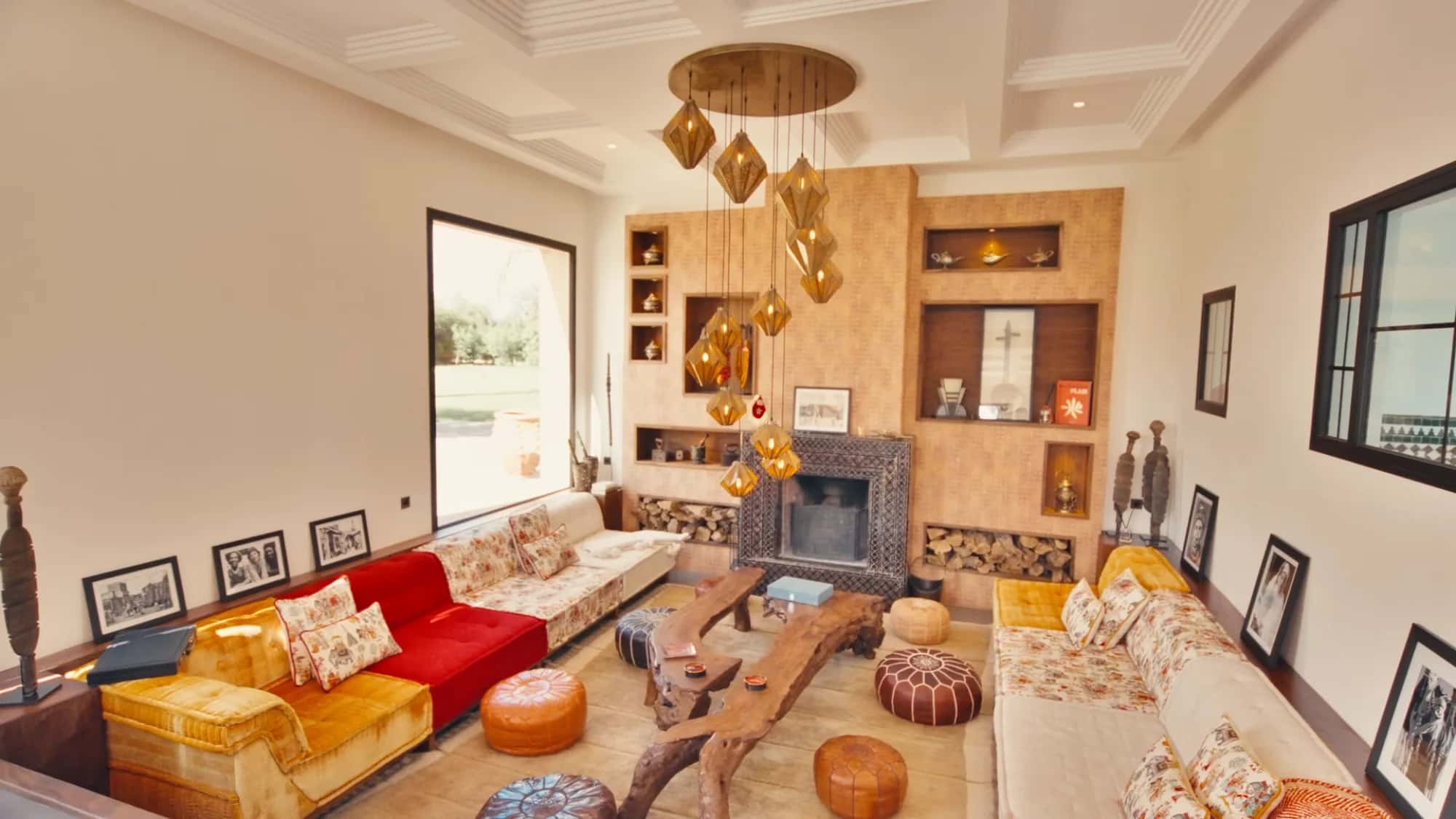 Villa Yemna riad lounge in Marrakech with red sofa, zellige fireplace, leather poufs and a cluster of copper pendant lights.