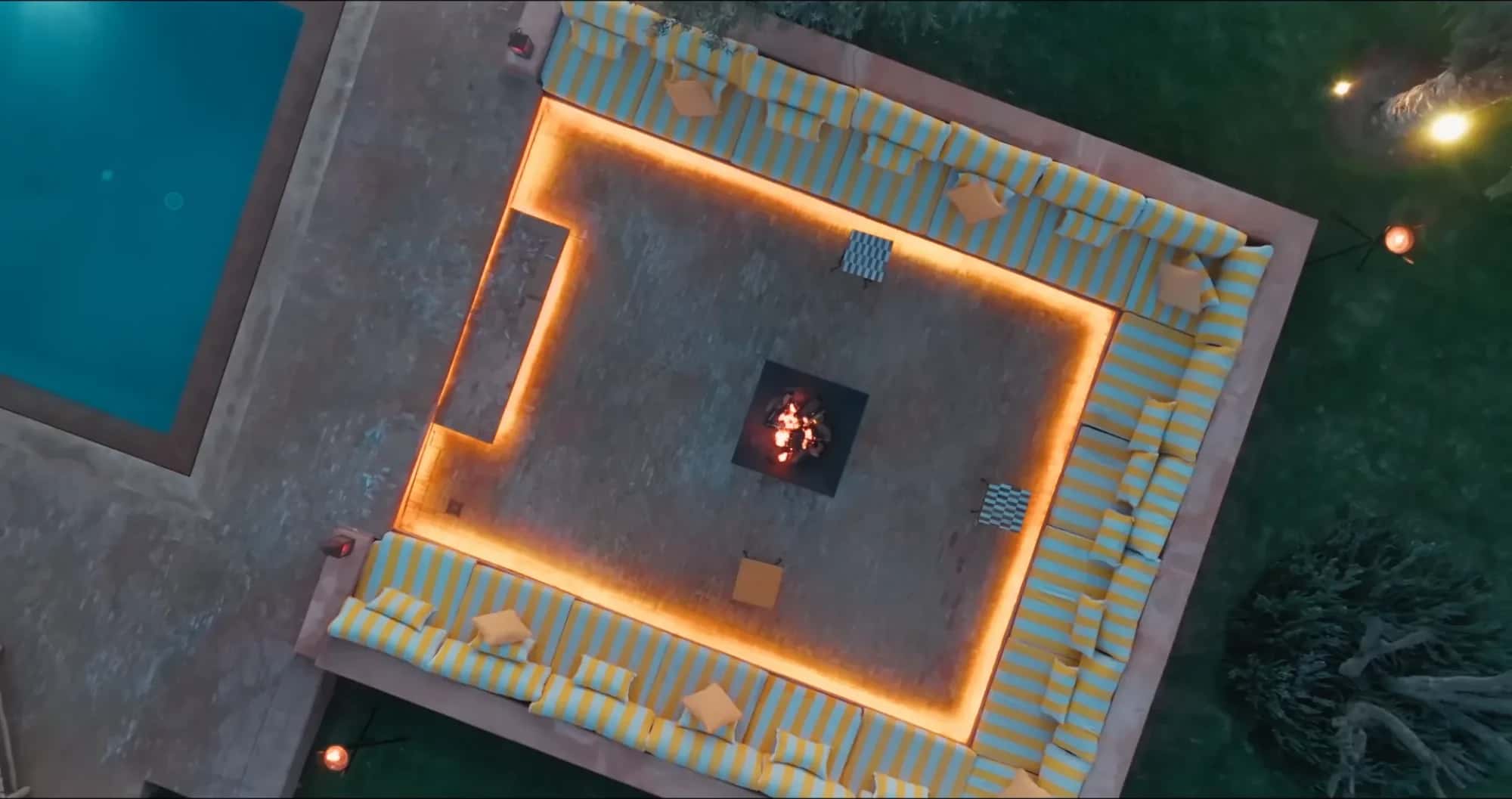 Aerial drone view of the Villa Yemna brasero lounge in Marrakech at twilight, with L-shaped seating, blue striped cushions and lit central fire pit.
