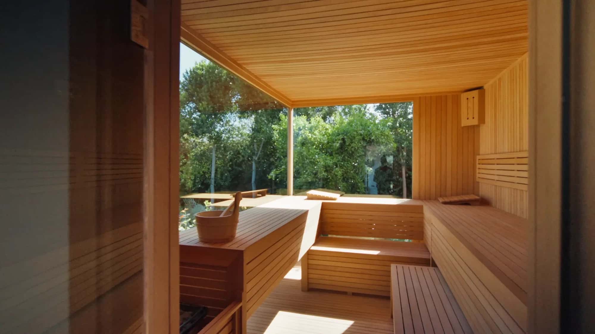 Private Villa Yemna sauna in Marrakech with light wood benches, paneled ceiling and large window opening onto the garden.