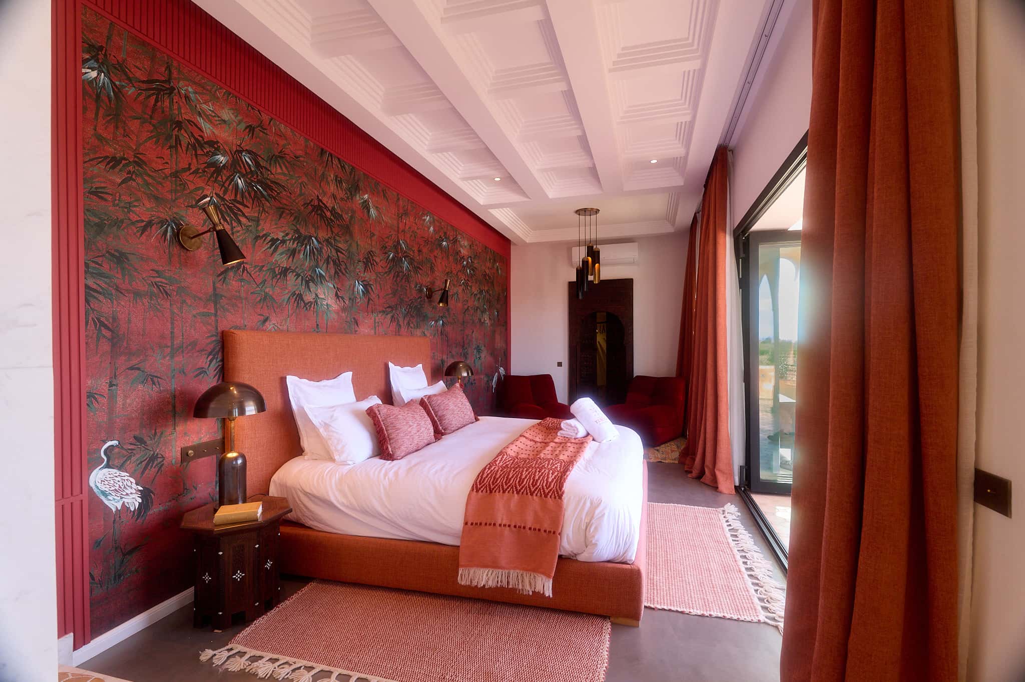 Side view of the Suite Oukaimeden at Villa Yemna, with a king-size bed, terracotta curtains, and glass doors toward the terrace.