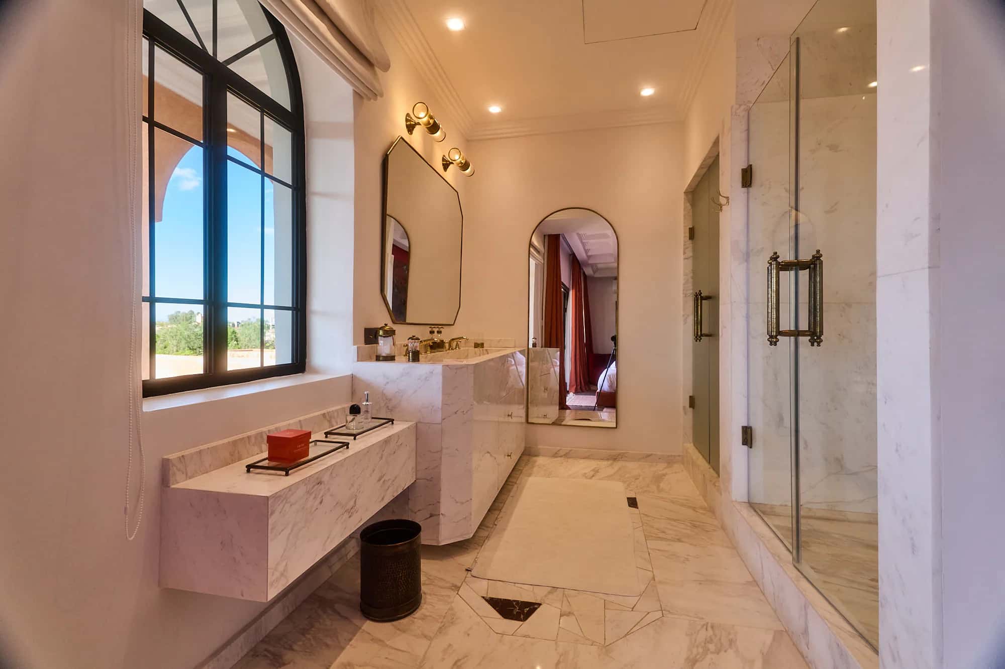 Large Villa Yemna marble bathroom with a double vanity, brass fixtures, glass shower, and full-height mirror.