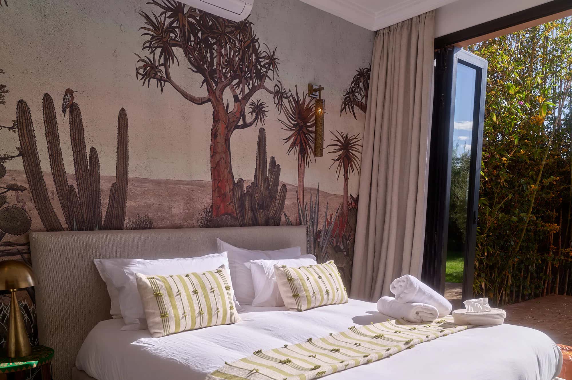 Villa Yemna suite bedroom with a cactus mural, bright white bedding, embroidered pillows, and an opening onto the private terrace.