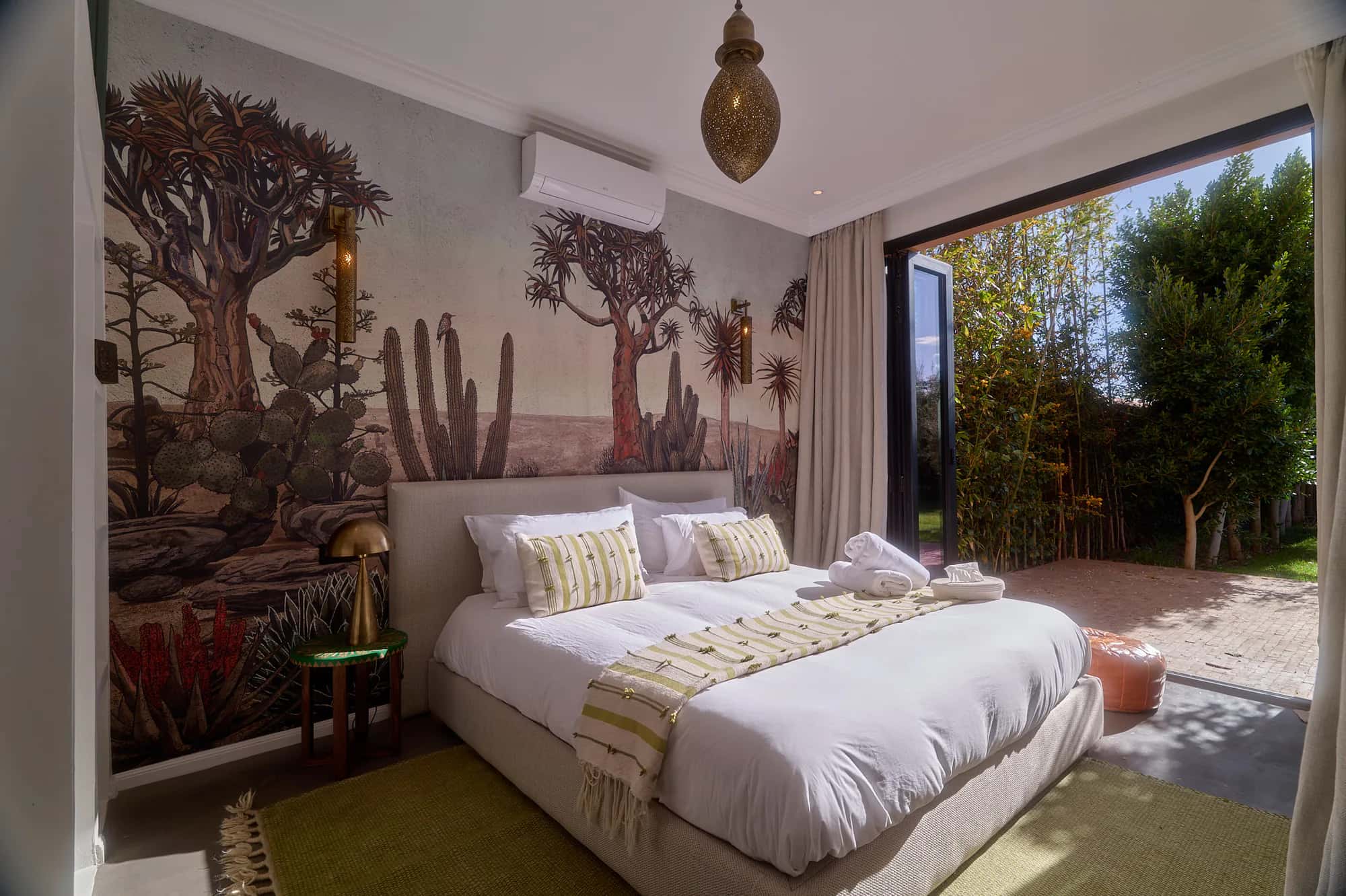 Independent Villa Yemna suite with a botanical wall mural, king-size bed, natural tones, and a glass door opening onto the garden.