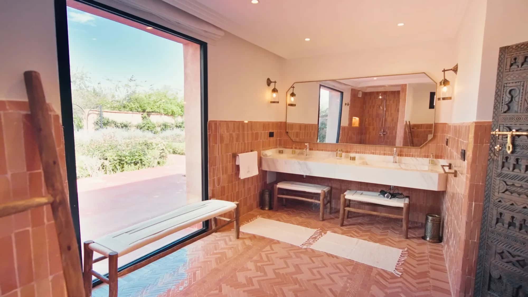 Villa Yemna suite bathroom in Marrakech with terracotta tiles, chevron flooring, marble double vanity and large garden-view opening.