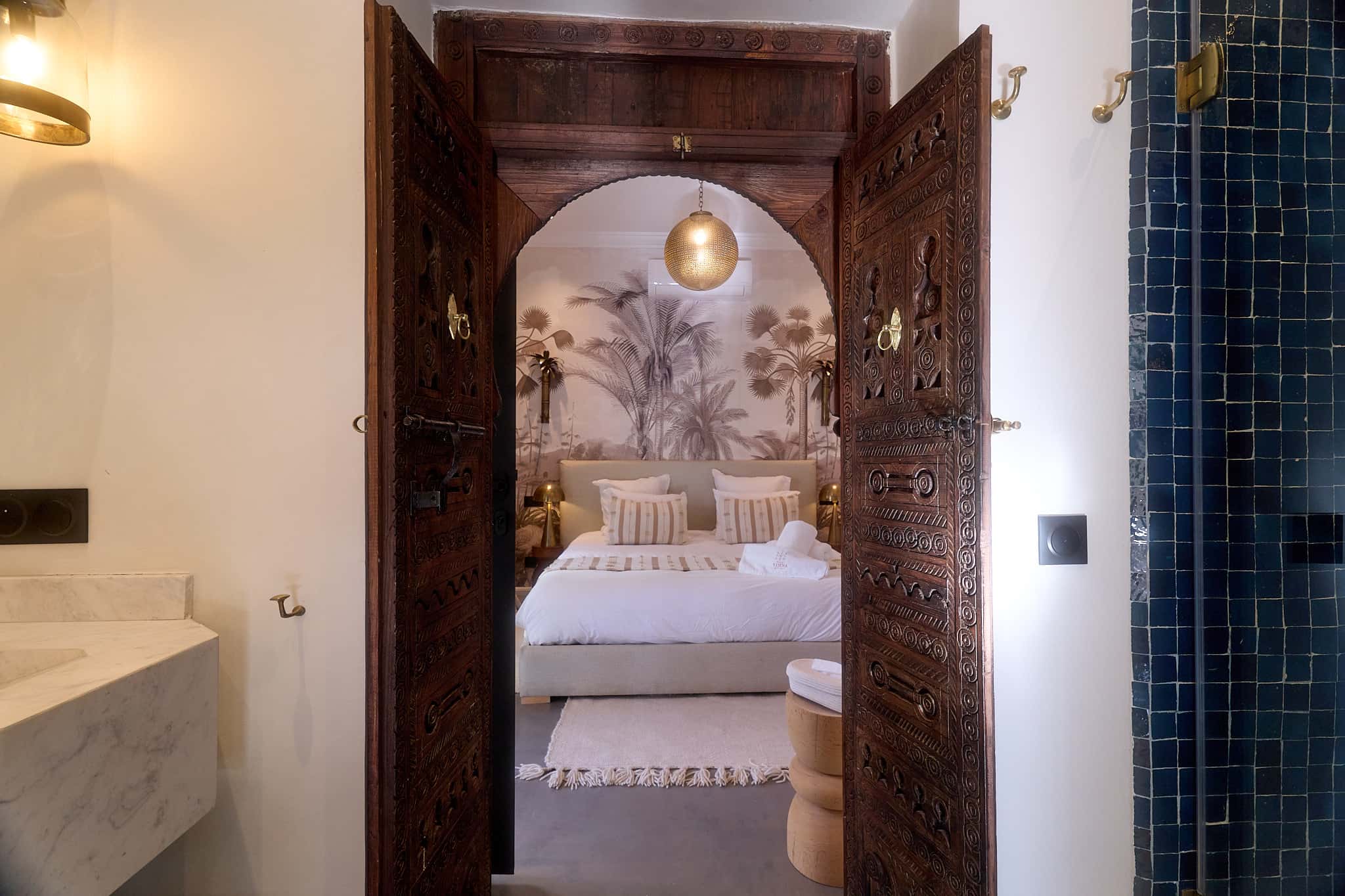 View of the Suite Ben Haddou bedroom from the shared bathroom, framed by carved Moroccan doors.