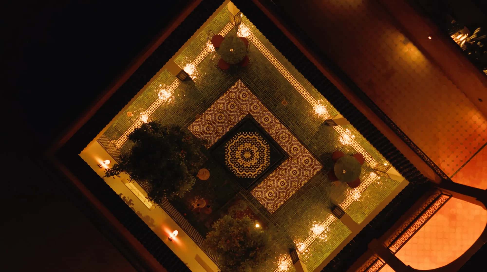 Night drone view of the illuminated riad courtyard with central fountain at Villa Yemna.
