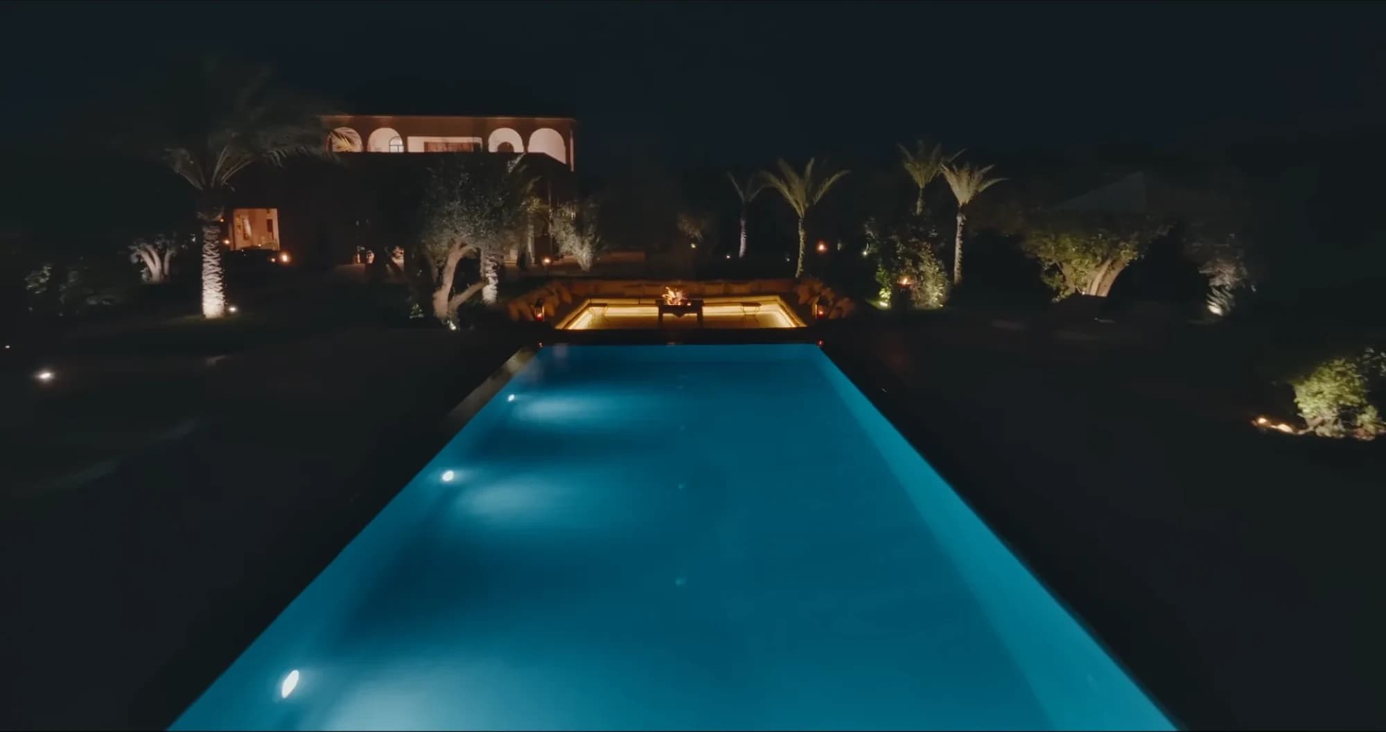 Villa Yemna pool in Marrakech illuminated at night, with lit riad in the background and palm trees.
