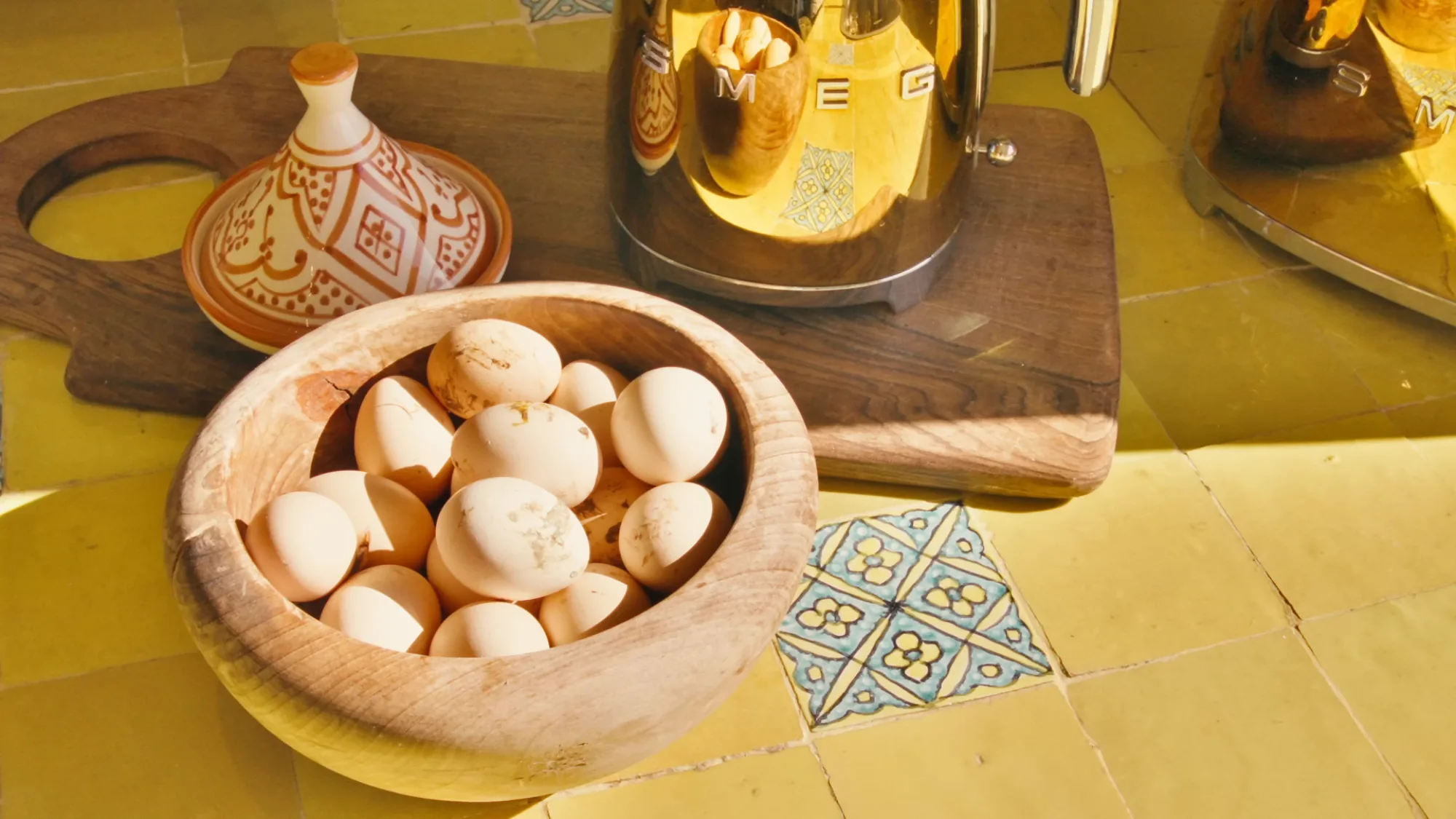 Kitchen detail at the Villa Yemna riad with wooden bowl of fresh eggs, gold SMEG kettle and yellow zellige countertop.