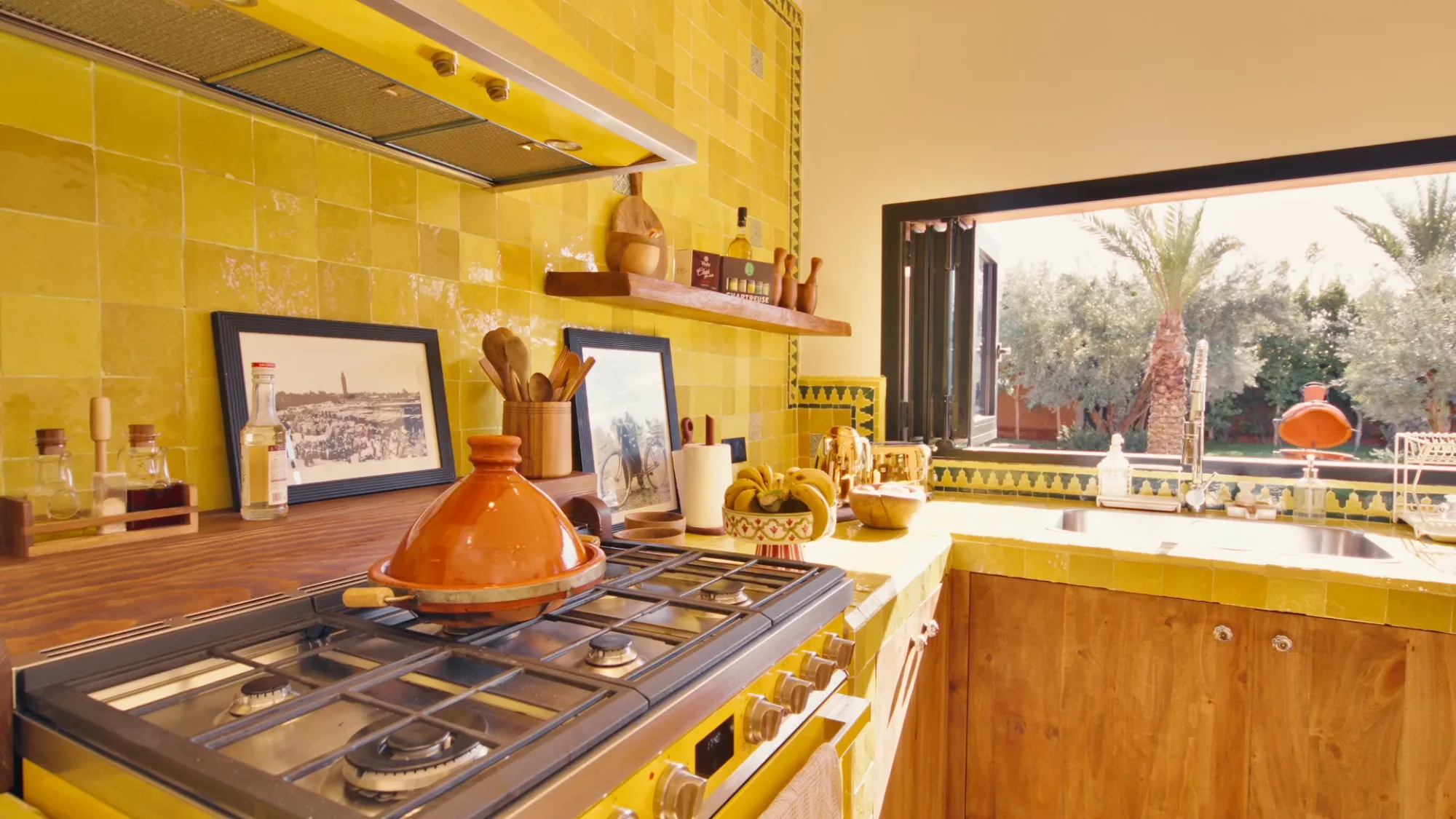 Villa Yemna riad kitchen in Marrakech with traditional orange tagine on the stove, shelves and yellow zellige tiles.