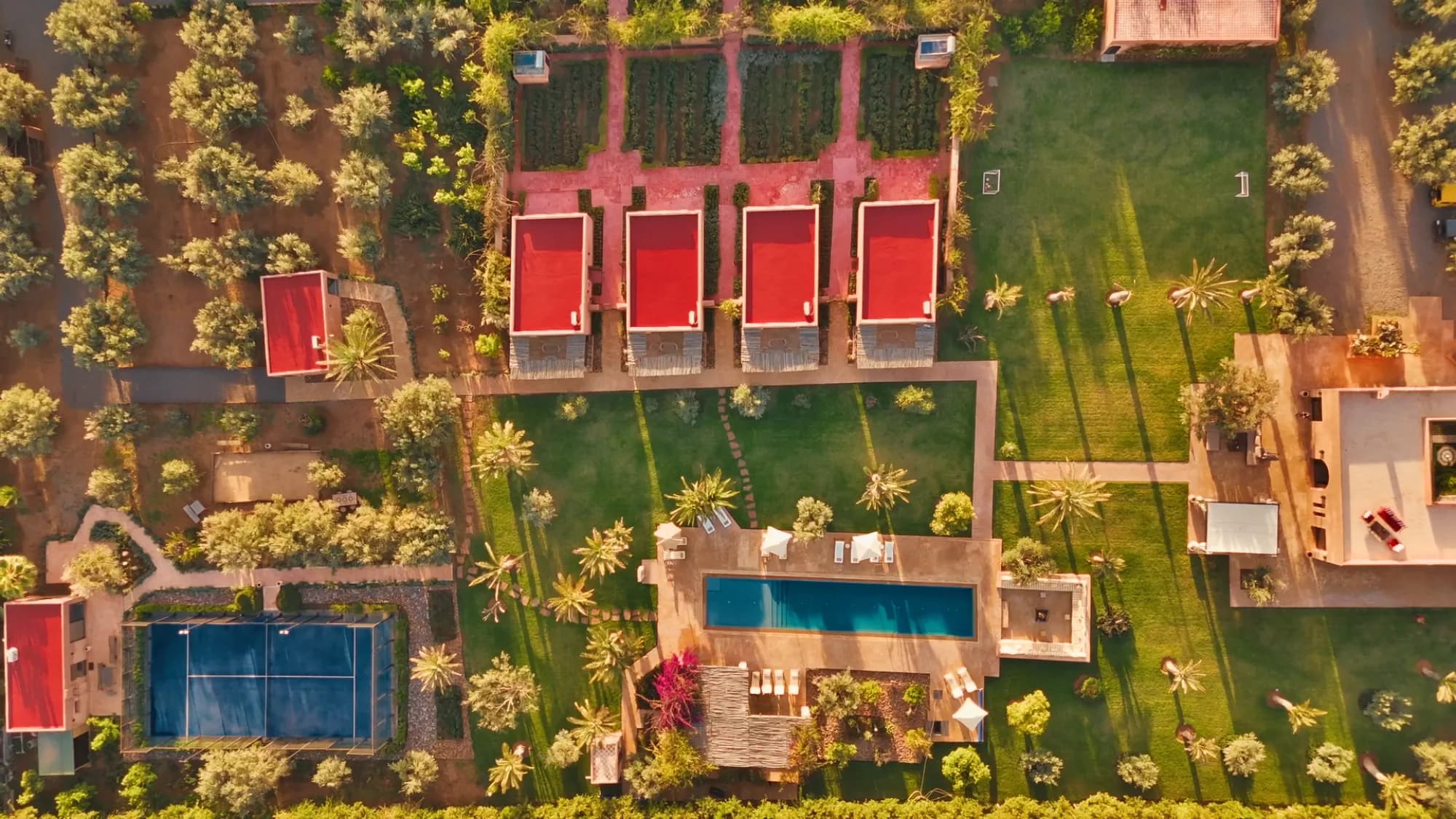 Aerial drone view of the entire Villa Yemna estate in Marrakech with the four red-roof bungalow suites, saltwater pool, padel court and gardens.