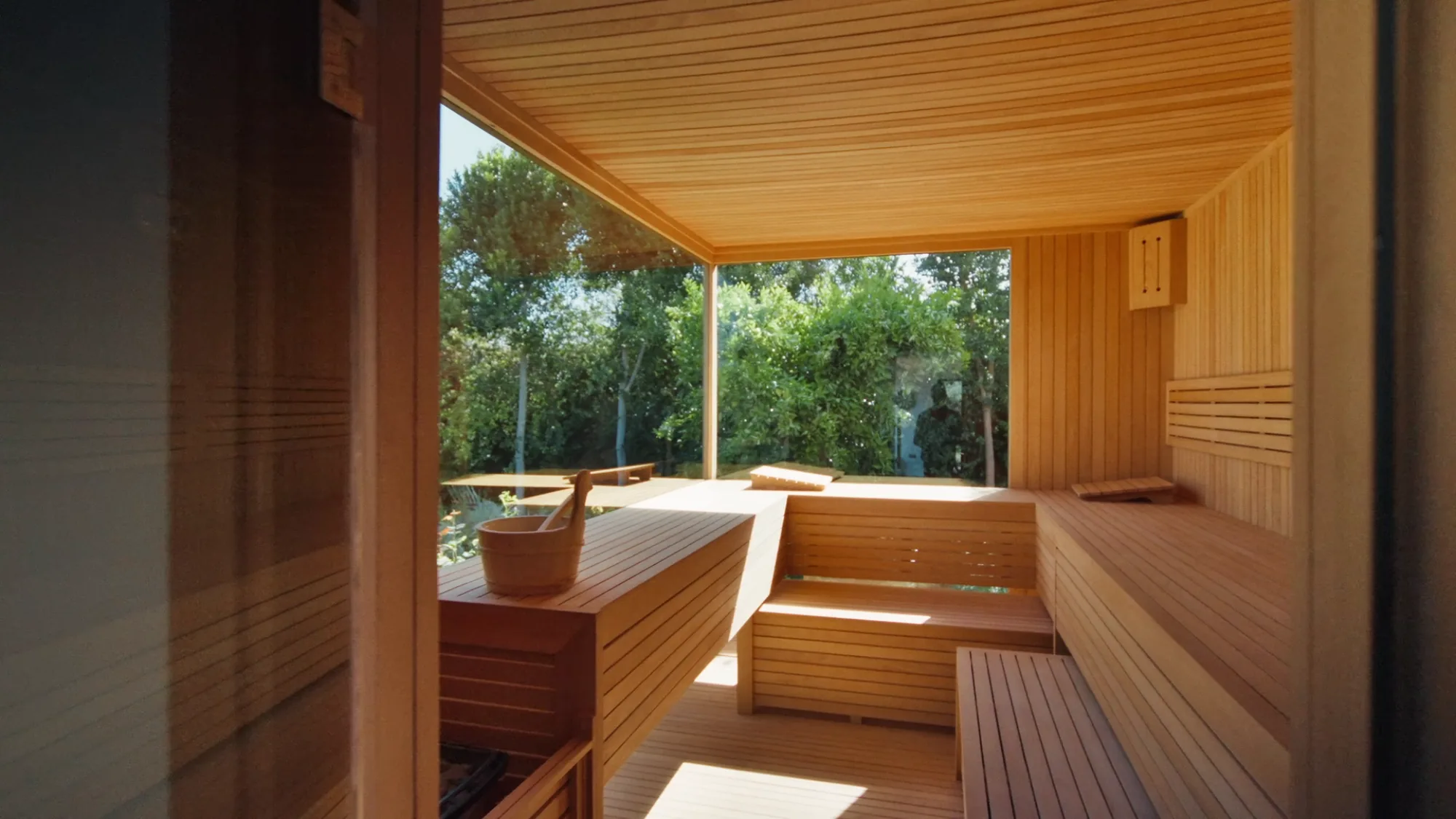 Private Villa Yemna sauna in Marrakech with light wood benches, paneled ceiling and large window opening onto the garden.