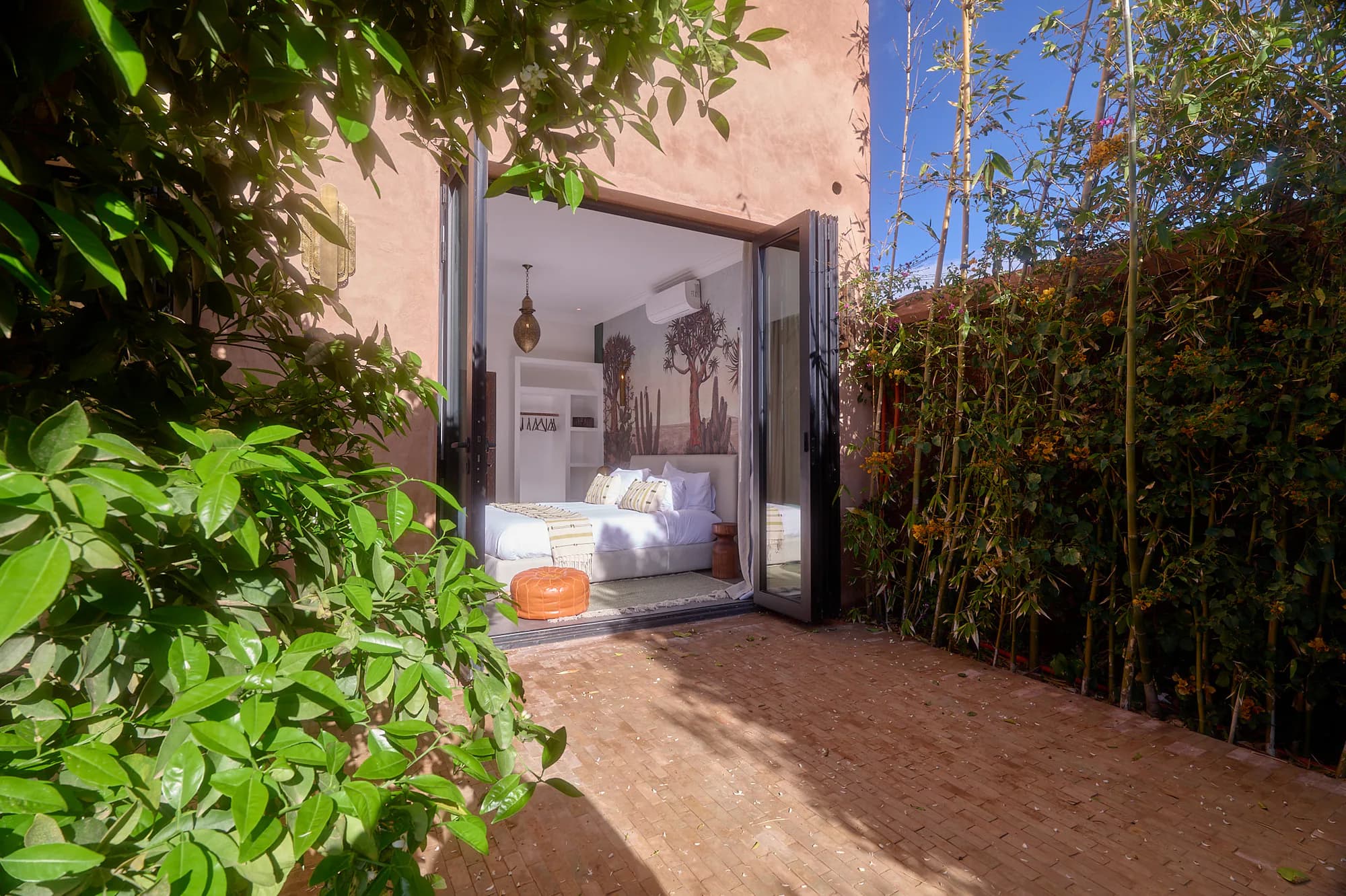 Private terrace of a Villa Yemna suite, framed by greenery, with wide glass doors opening onto a bright bedroom.